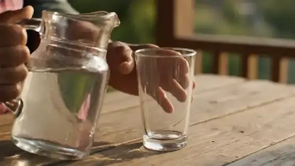 A hand pouring water from a glass pitcher into a tall glass on a porch table